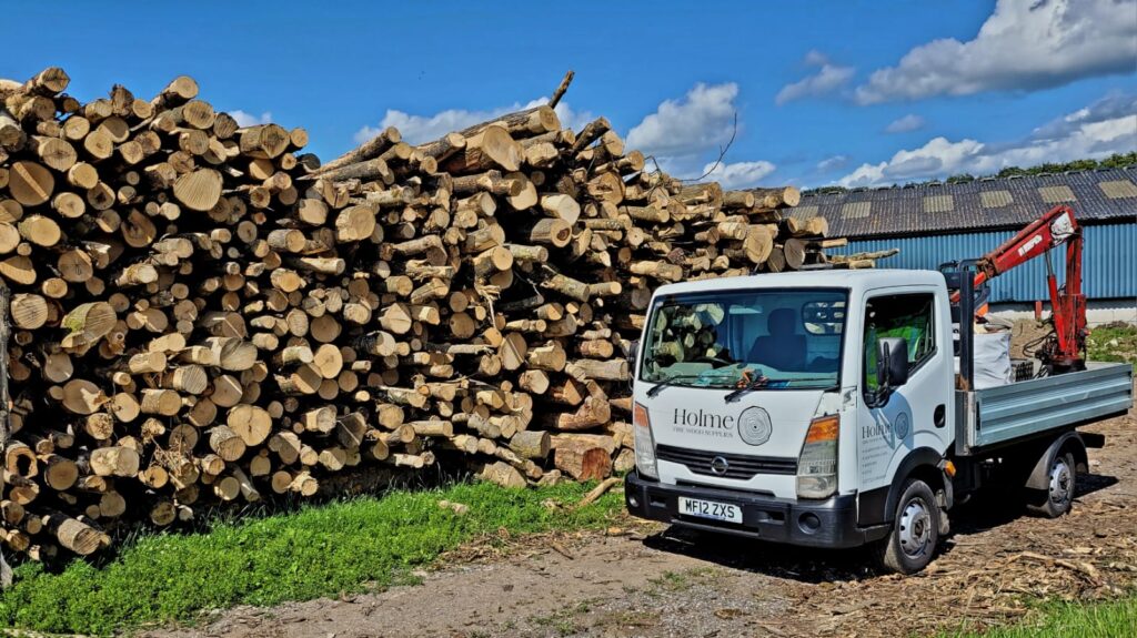 Home Firewood delivery truck next to stacks of hardwood firewood logs